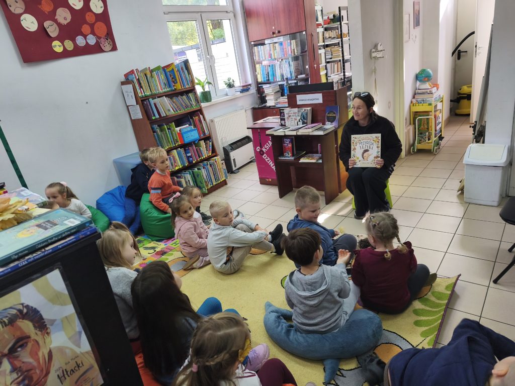 Bibliotekarz-pokazuje-czytana-ksiazke-dzieci-siedza-na-dywanie-i-sluchaja