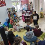 Bibliotekarz-pokazuje-czytana-ksiazke-dzieci-siedza-na-dywanie-i-sluchaja