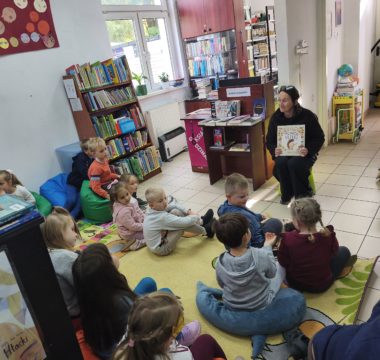 Bibliotekarz-pokazuje-czytana-ksiazke-dzieci-siedza-na-dywanie-i-sluchaja
