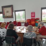 Siedem kobiet siedzi przy dużym stole zastawionym filiżankami oraz ciastem i rozmawia o książce